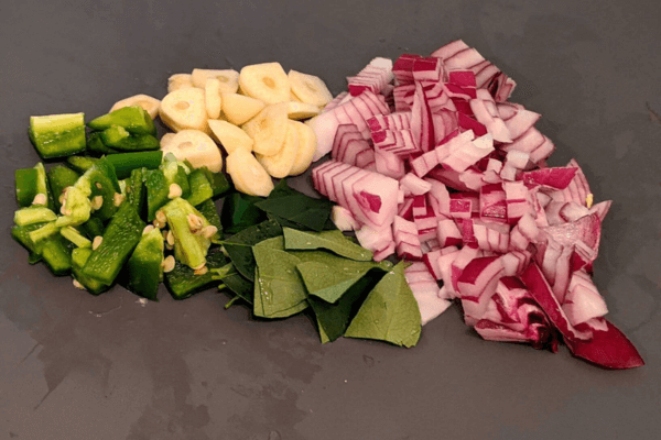 chopped onions, garlic, green chillies and curry leaves on a gray cutting board