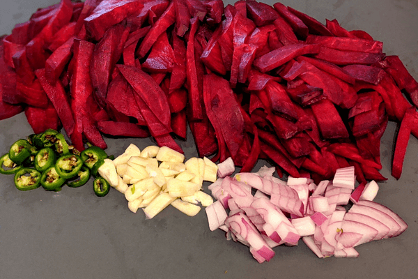 Two large cleaned beets, half a red onion, two garlic cloves and one thai chili, all chopped on a cutting board