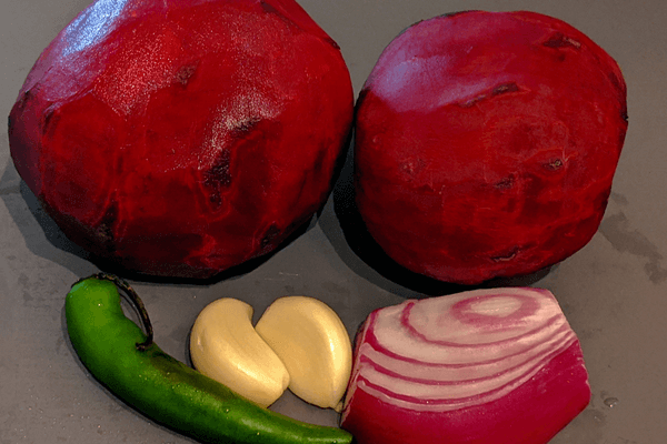 Two large cleaned beets, half a red onion, two garlic cloves and one thai chili on a cutting board