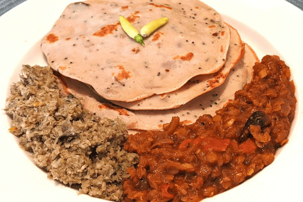 Two green chilies sitting on a stack of dosas on a white plate. Sambol and curry also on one side of the plate