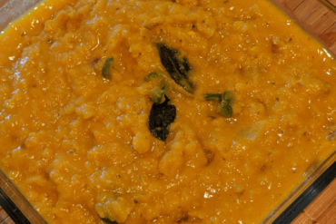Creamy lentil curry soup topped with curry leaves on a glass dish