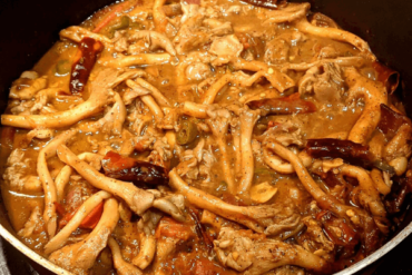 Oyster mushrooms in a dark curry with dried chilies on a pan