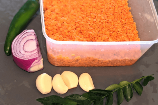 red lentils, onion, garlic cloves, and curry leaves on a cutting board