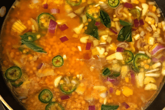 Red split lentils being boiled in a pan with water, chopped onions, garlic and chillies