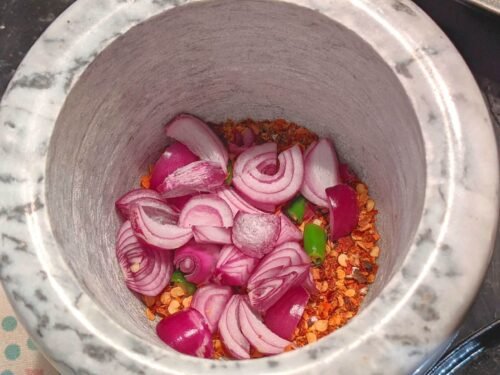 red chilli flakes and chopped red onions inside a mortar
