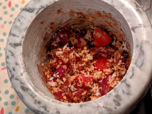 pol sambol ingredients being chopped with a mortar and pestle