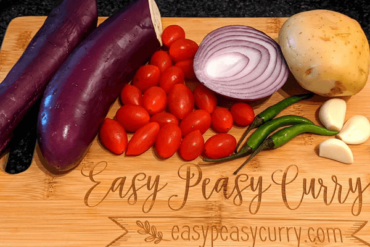 potato, aubergine, cherry tomatoes, onions, garlic and green chilies on a cutting board