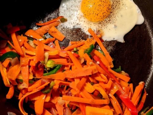 Fried vegetables on one side of a pan with a fried egg on the other side