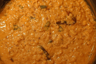 Red split lentil or dhal curry in a pan topped with dried chilies