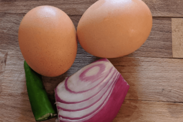 two eggs, red onion and green chillies on a cutting board