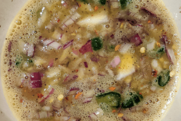 Beaten egg with spices and chopped vegetables in a bowl