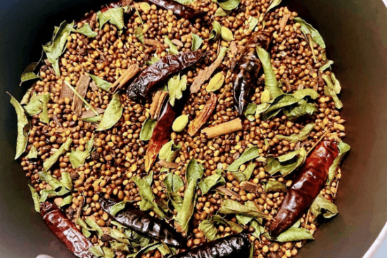 Whole spices roasted on a pan. Spices include corriander, dried chilies, curry leaves, cinnamon