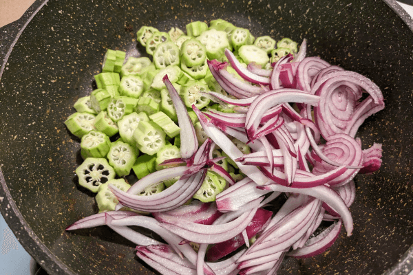 Chopped ladies fingers and onions on a cooking pan