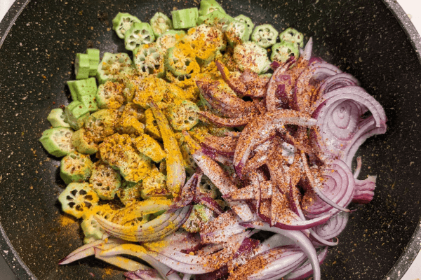 Chopped ladies fingers, onions and spices on a cooking pan