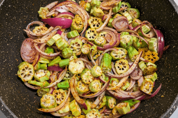 Chopped ladies fingers, onions and spices on a cooking pan