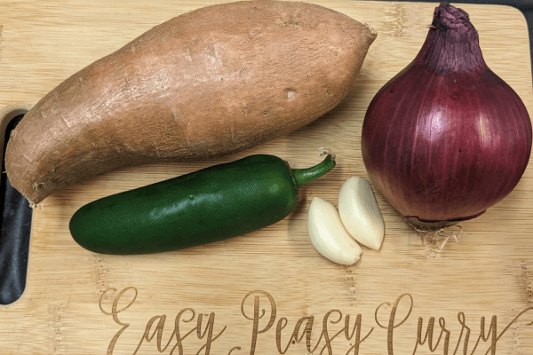 sweet potato, red onion, jalapeno and two garlic cloves on a cutting board